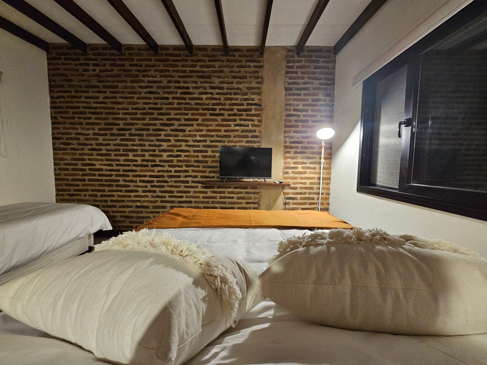 Cama matrimonial frente a la pared de ladrillo